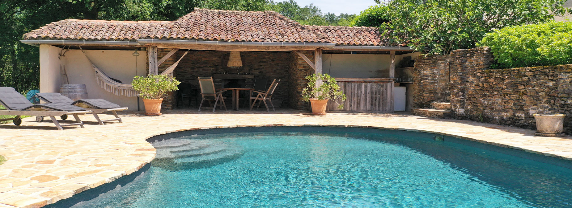 Zwembad en terras van luxe vakantiehuis in Dordogne, omgeven door groene tuin en rustieke sfeer.