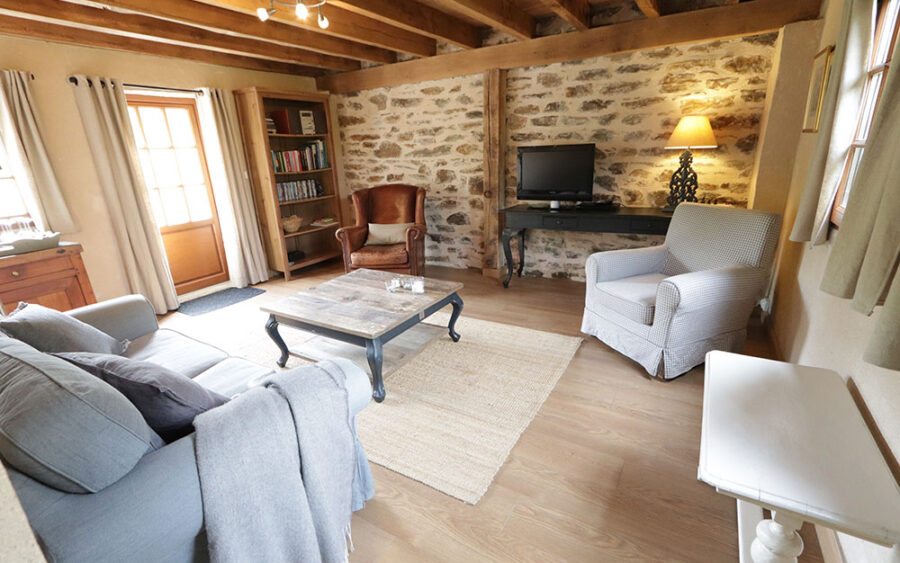 Luxe Vakantiewoonkamer Dordogne Gezellige woonkamer in luxe vakantiehuis in Dordogne met comfortabele zitplaatsen en rustieke stenen.