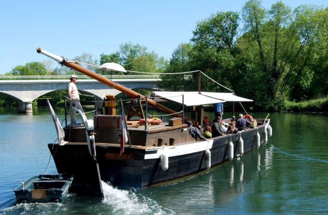 Een authentieke gabarre vaart rustig over de Charente, omringd door groen glooiend landschap en historische plekken, perfect voor een culturele ervaring.