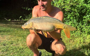 Vissen vangen in Dordogne Man met grote vis in tuin, omgeven door groen, zonnige dag.
