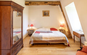 Cozy bedroom with rustic wooden beams, double bed, and warm lighting in a Dordogne vacation house.