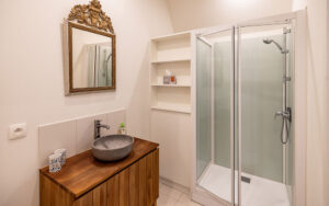 Modern bathroom with shower, wooden vanity, and decorative mirror in Dordogne vacation home.
