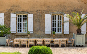 Outdoor dining setup with rustic charm, featuring a long wooden table and white shutters in a pictur.