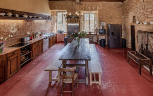 Rustic kitchen with wooden cabinets, stone walls, and large windows in Dordogne.