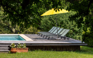 Outdoor pool with sun loungers and yellow umbrella in lush garden.