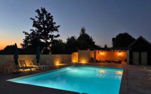 Zwembad bij zonsondergang in luxe vakantiehuis in Dordogne, met comfortabele ligstoelen en sfeervoll.