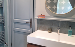 Bright bathroom featuring a stylish wooden vanity, round mirror, and soft blue walls. Perfect for re.