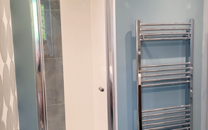 Bathroom shower with glass door, blue wall, and chrome towel radiator.