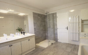 Modern luxury bathroom with double sink, large mirror, walk-in shower, and stylish decor.