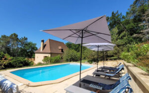 Bright swimming pool with sun loungers and umbrellas in scenic Dordogne countryside.