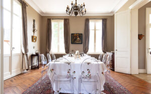 Luxe eetkamer met grote ramen, chandelier en klassieke decoratie.