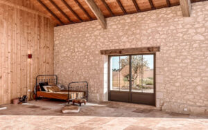 Luxe Vakantiehuis Dordogne interieur Ruime slaapkamer met stenen muur en grote ramen in Dordogne vakantiehuis.