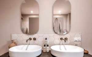 Moderne badkamer in Luxe Vakantiehuis Twee witte wastafels met ovalen spiegels in een luxe badkamer.